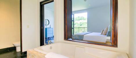 A bathroom with a large bathtub, a toilet, and a mirror.