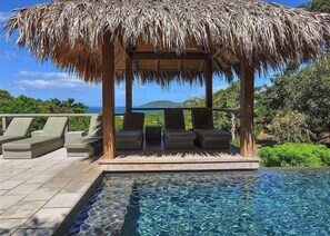 A pool area with a thatched roof structure, lounge chairs, and a view of the ocean. - Las Mareas Villa 1 (Tamarindo)