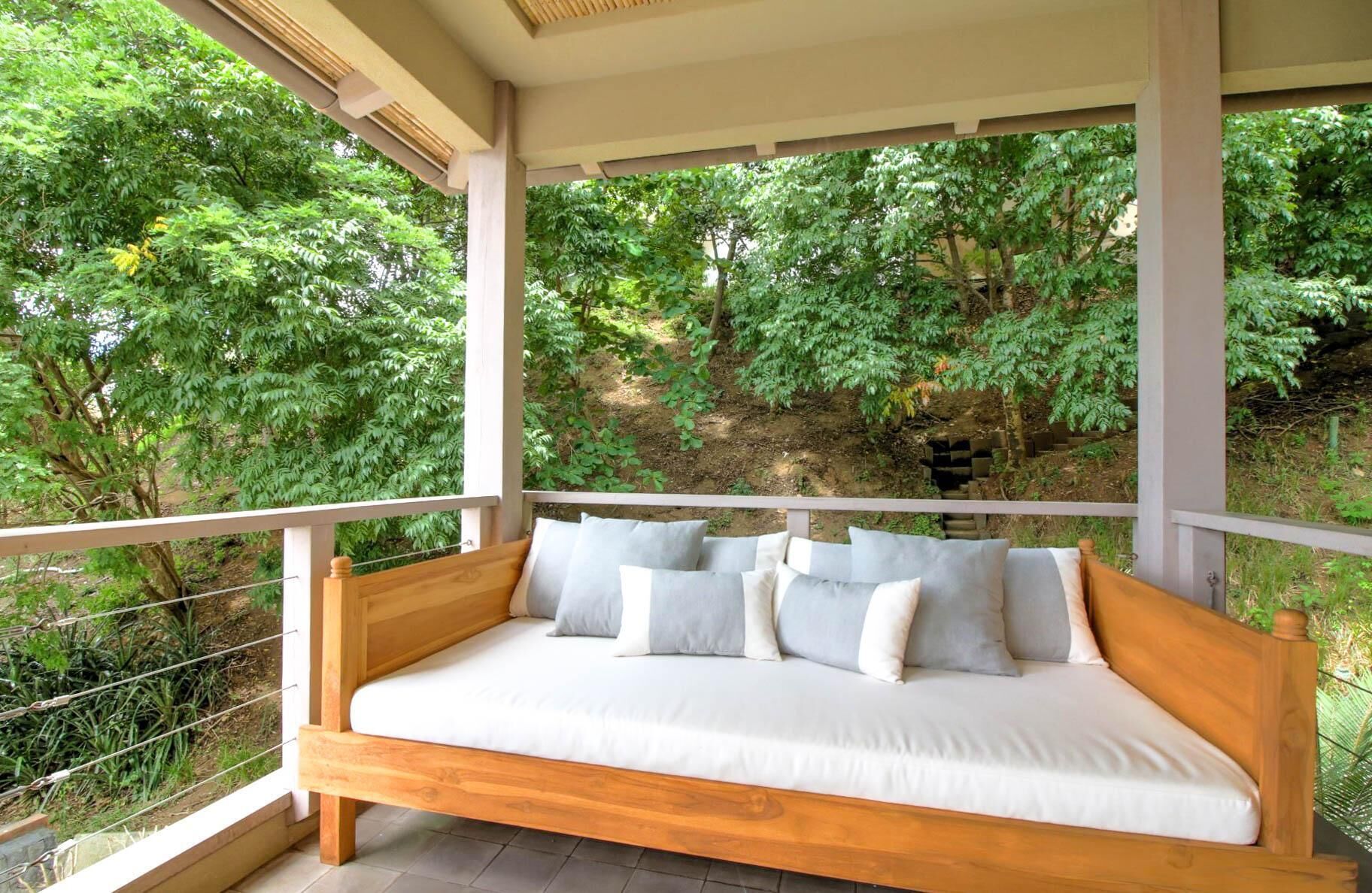 A wooden bench with cushions, overlooking a lush garden and trees.