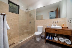 A modern bathroom with a glass-enclosed shower, a white toilet, a wooden vanity with a sink, and a large mirror. - Las Mareas Villa 1 (Tamarindo)