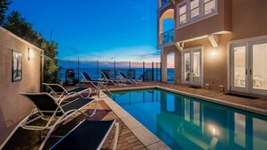 Un espace piscine avec des chaises longues et une vue sur l’océan au crépuscule.