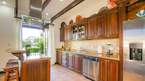 A modern kitchen with wooden cabinets, a granite countertop, stainless steel appliances, and a large island with a sink. - Villa Mansita (Tamarindo)