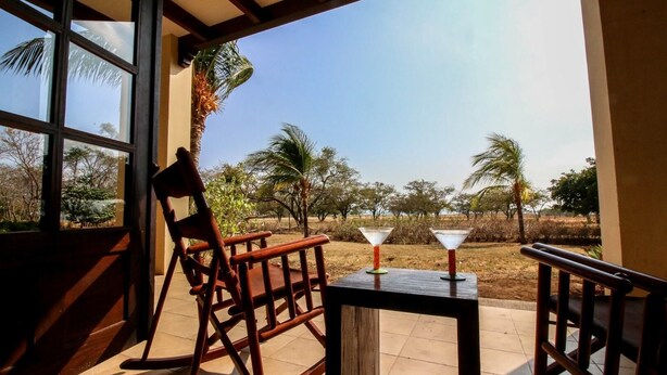 A wooden rocking chair and a small table with two martini glasses on a balcony with a view of palm trees and a clear sky. - Villa Mansita (Tamarindo)