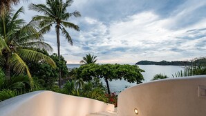 A staircase leading to a balcony overlooking a body of water, surrounded by lush greenery and palm trees. - Flamingo Blu (Cabo Velas)