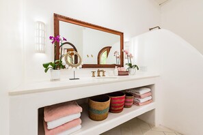 A bathroom vanity with a large mirror, a sink, and a shelf below holding towels and baskets.