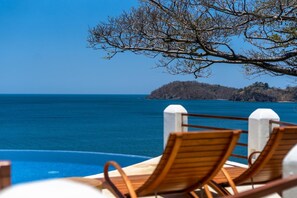 A poolside area with wooden lounge chairs and a view of the sea and a distant island.