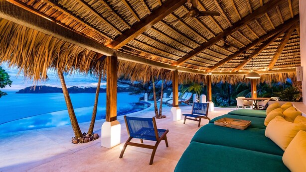 An outdoor lounge area with a thatched roof, lounge chairs, and a view of the sea. - Flamingo Blu (Cabo Velas)