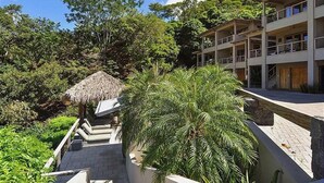Un hotel con una estructura de techo de paja, rodeado de exuberante vegetación y un edificio de varios pisos con balcones.