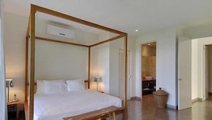 Una cama con dosel sobre un armazón de madera, una mesita de noche, una lámpara y un banco.