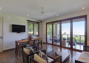 A spacious living area with a dining table, chairs, a sofa, and a TV mounted on the wall.
