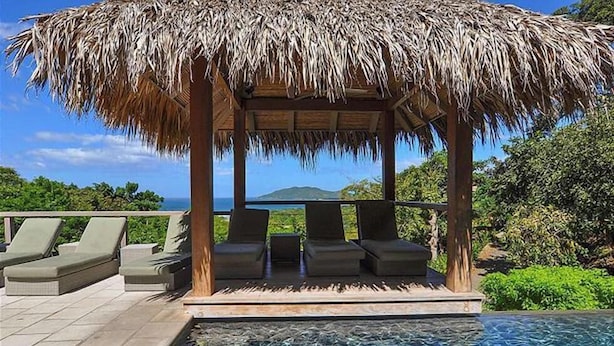 Un pabellón de techo de paja con sillones de descanso con vistas a una piscina.