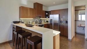 Una cocina moderna con una isla central, taburetes de bar, electrodomésticos de acero inoxidable y armarios de madera.