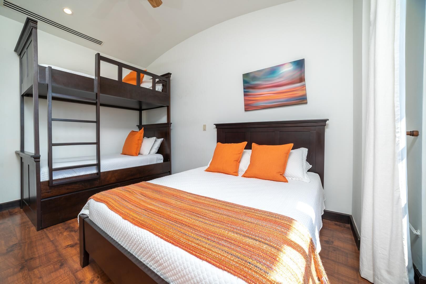 Een hotelkamer met een stapelbed, een groot bed met oranje kussens, een schilderij aan de muur en een houten vloer.