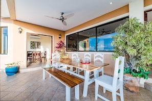 A dining area with a wooden table and white chairs, a ceiling fan, and potted plants.