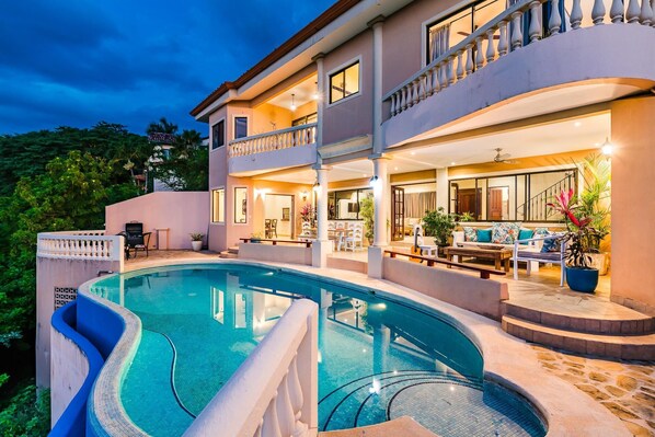 A two-story house with a swimming pool, outdoor seating, and a balcony.