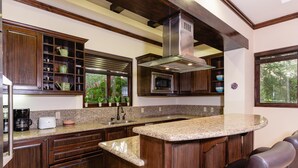 A kitchen with wooden cabinets, a granite countertop, a built-in microwave, and a large window with a view of greenery. - Villa Lucia (Tamarindo)