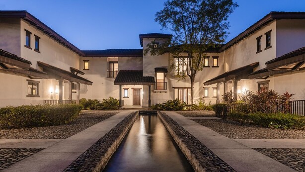 A courtyard with a central water feature, surrounded by buildings with balconies and windows. - Villa Lucia (Tamarindo)