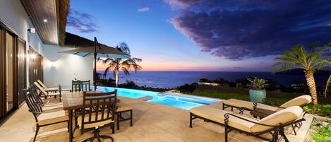An outdoor pool area with lounge chairs and a dining set, overlooking a scenic view.