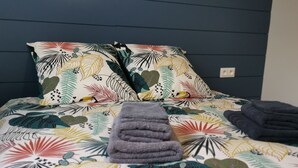 Ein Bett mit einer farbenfrohen Bettdecke mit Blattmuster, zwei Kissen und einem gefalteten grauen Handtuch.
