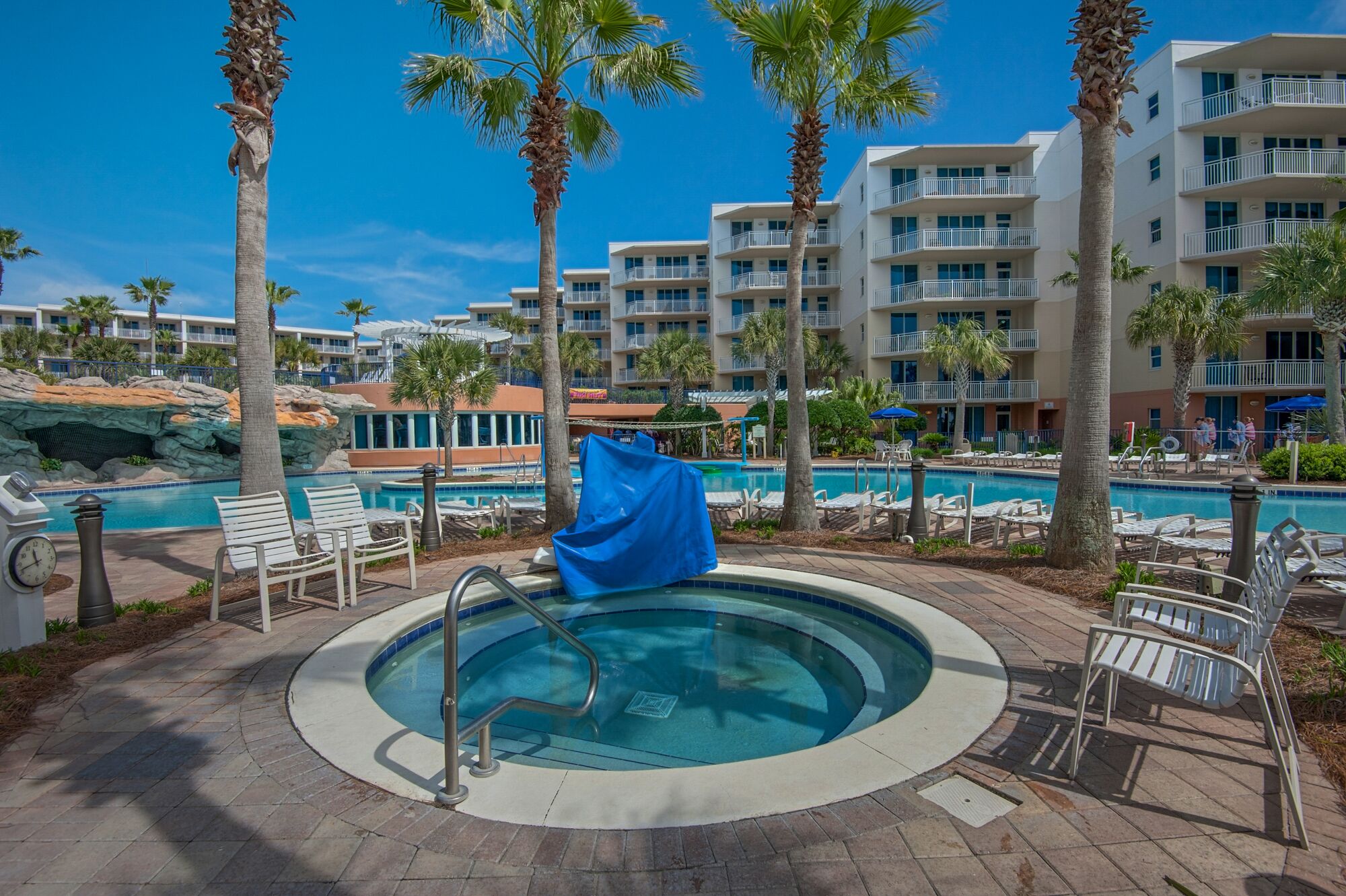 A pool area with lounge chairs, a hot tub, and palm trees.