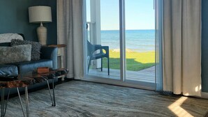 A living room with a view of the sea, a sofa, a lamp, and a chair by the window. - Islands View Condo- Waterfront (Saint Ignace)