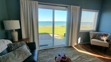 A room with a view of the sea, a sofa, a chair, and a lamp.