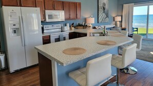 A modern kitchen with a central island, white appliances, and a view of the ocean. - Islands View Condo- Waterfront (Saint Ignace)