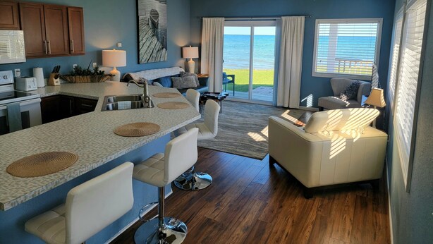 A modern kitchen with a bar area, a dining space, and a living area with a view of the ocean. - Islands View Condo- Waterfront (Saint Ignace)
