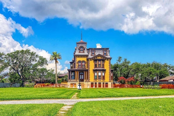 A large, historic building with a prominent tower, surrounded by a well-maintained lawn and trees.