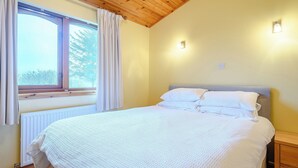 Une chambre avec un plafond en bois, une grande fenêtre avec des rideaux, un lit avec une literie blanche et une table de chevet.