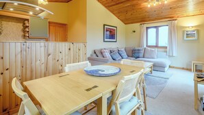 Une pièce chaleureuse avec un plafond en bois, une table à manger avec des chaises, un canapé et une fenêtre avec des rideaux.