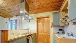 Une cuisine avec des meubles de rangement en bois, une hotte de cuisine en acier inoxydable, un four encastré et une fenêtre avec des rideaux.
