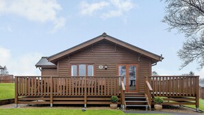 Une cabane en bois avec une véranda, une porte d’entrée et un petit jardin devant, agrémenté de deux plantes en pot.