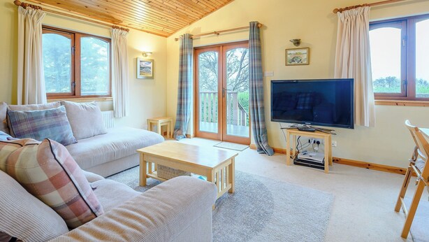 Un salon chaleureux avec un plafond en bois, un canapé, une table basse, un téléviseur et de grandes fenêtres avec des rideaux.