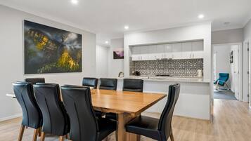 A modern dining area with a wooden table and black chairs, a kitchen with patterned backsplash, and a large abstract painting on the wall.