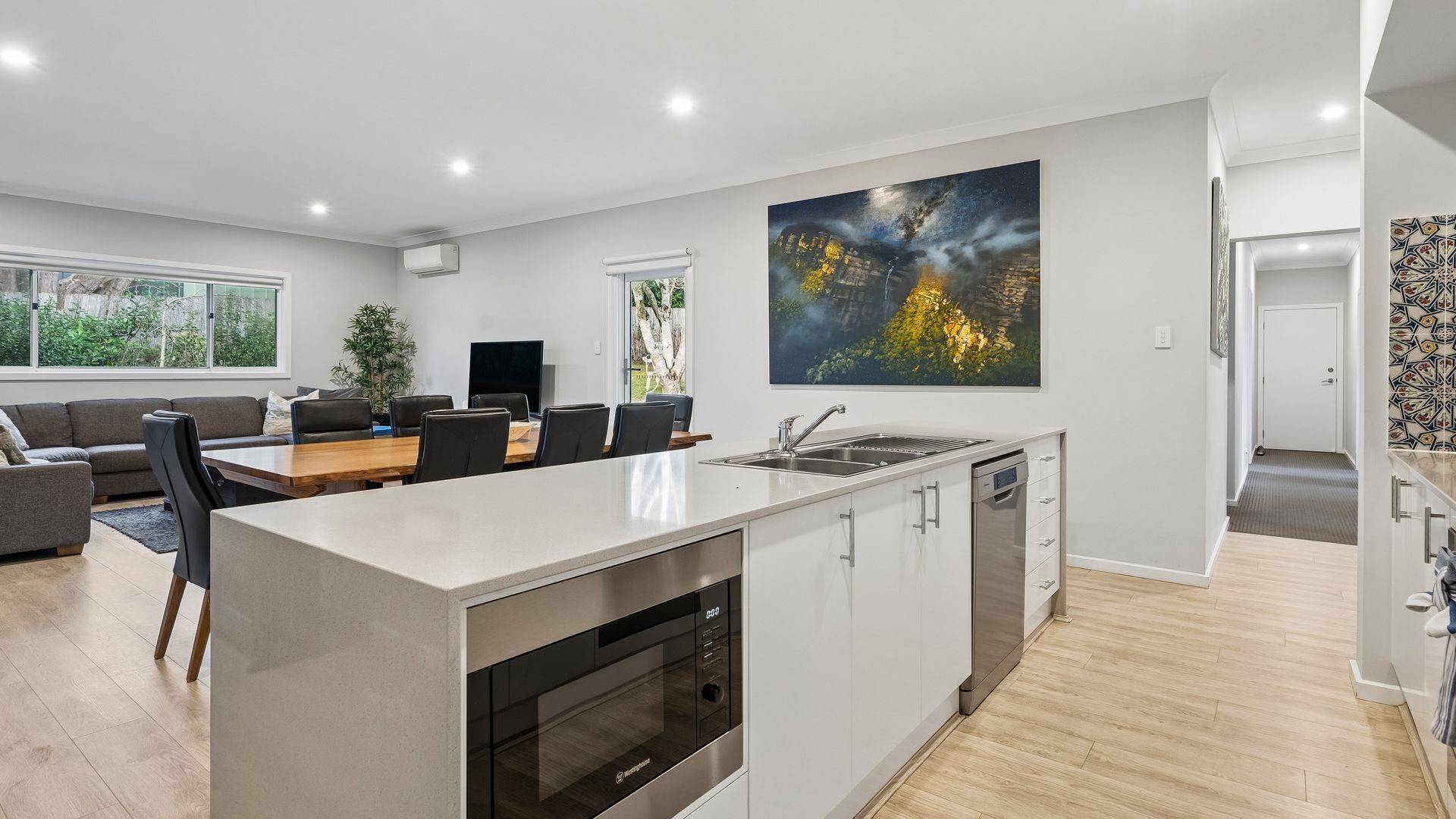 A modern kitchen with a central island, a dining area with a gray sofa, and a large window.
