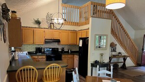 A kitchen with wooden cabinets, a black refrigerator, a stove, and a dining area with two wooden chairs and a table. - LAKEFRONT HARTWELL! Good dogs welcome! Covered dock, fire pit, kayaks! (Westminster)