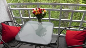 Una mesa con cubierta de vidrio, dos cojines rojos, un florero con flores y una barandilla blanca.