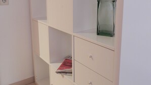 Un armario blanco con varios estantes y cajones, un florero de vidrio en el estante superior y un libro en el estante inferior.