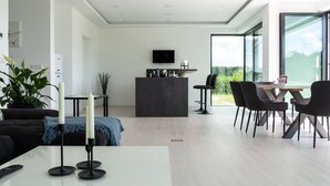 Ein modernes Wohnzimmer mit Essbereich, einem wandmontierten Flachbildfernseher und einem großen Fenster mit Blick ins Freie.