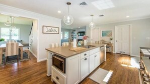 Una cocina moderna con una isla central, iluminación colgante y vistas al comedor.