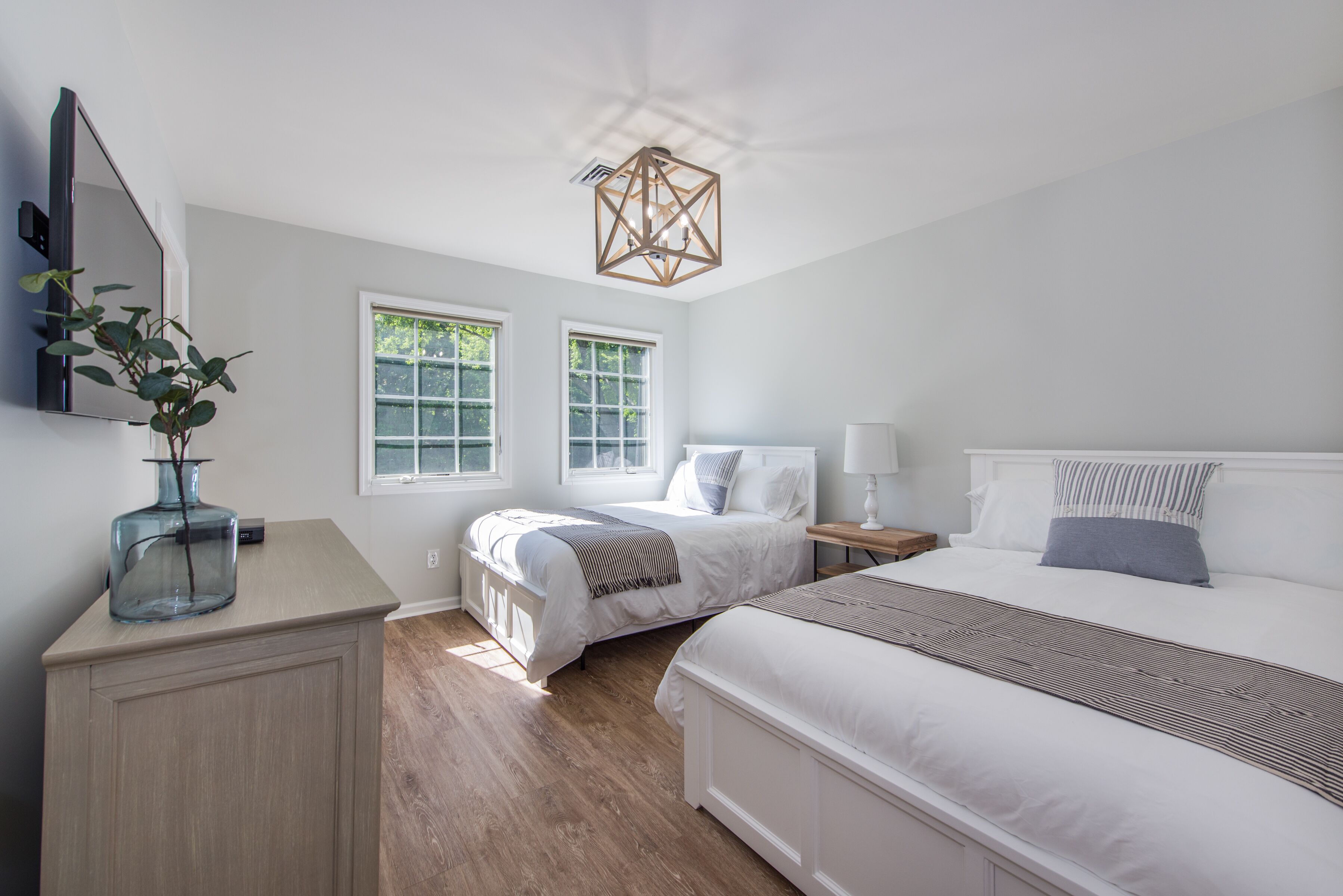 Une chambre avec deux lits, une commode, un miroir et un luminaire au plafond de forme géométrique.