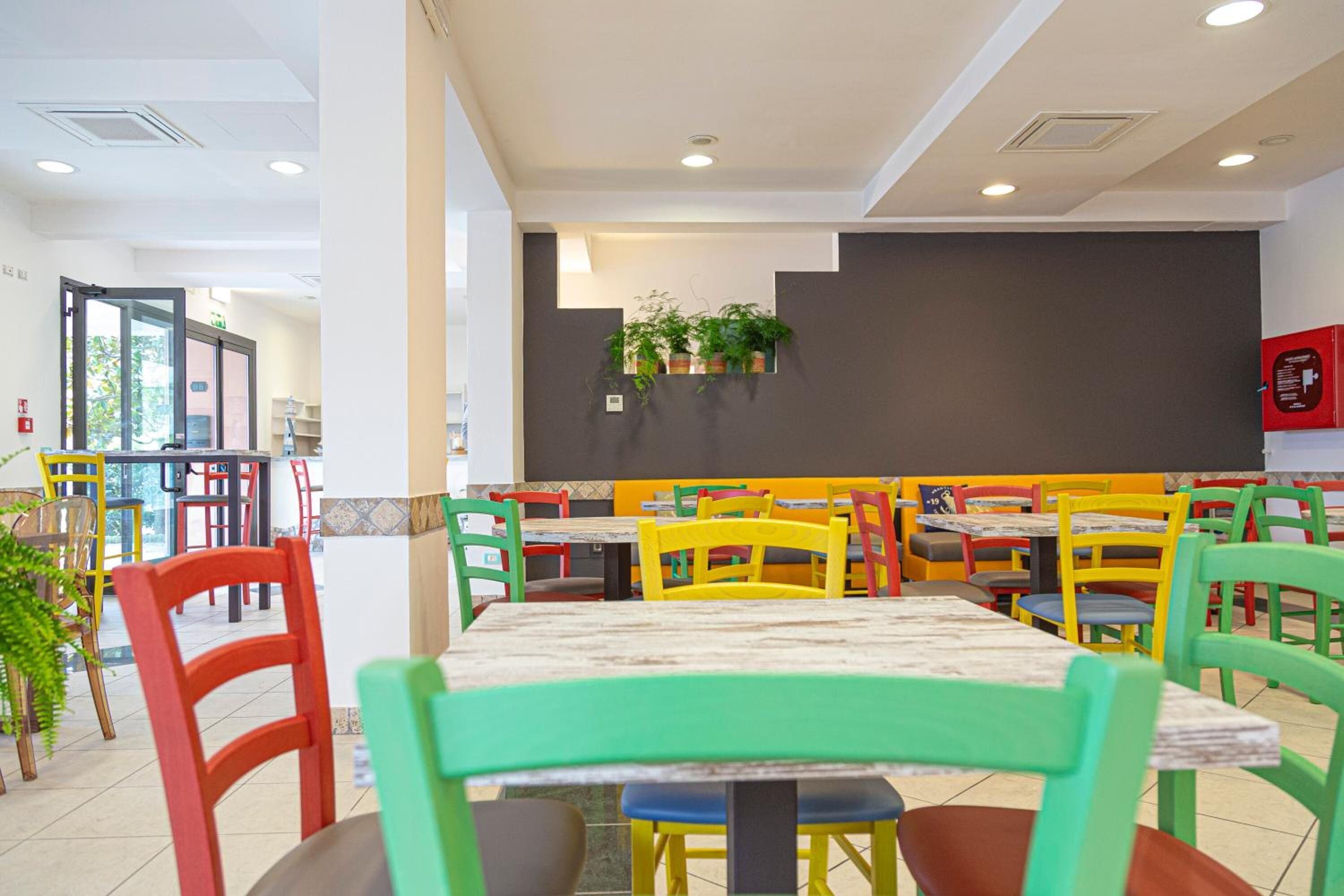 A restaurant with colorful chairs and tables, a blackboard on the wall, and a fire extinguisher.