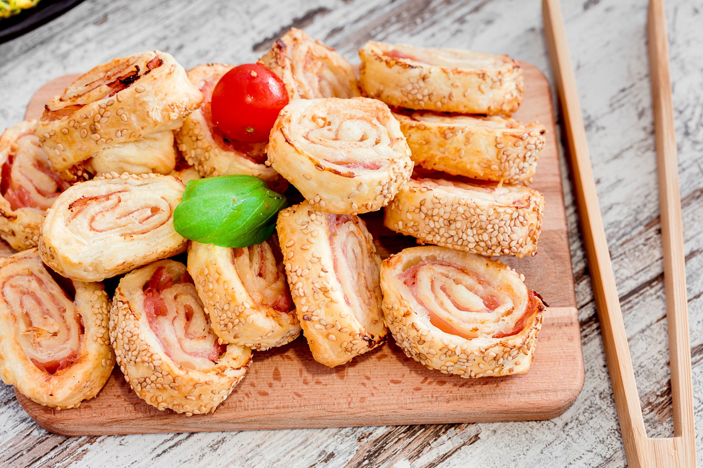 Une planche en bois sur laquelle sont disposées plusieurs pâtisseries, dont une tomate cerise et une feuille de basilic.