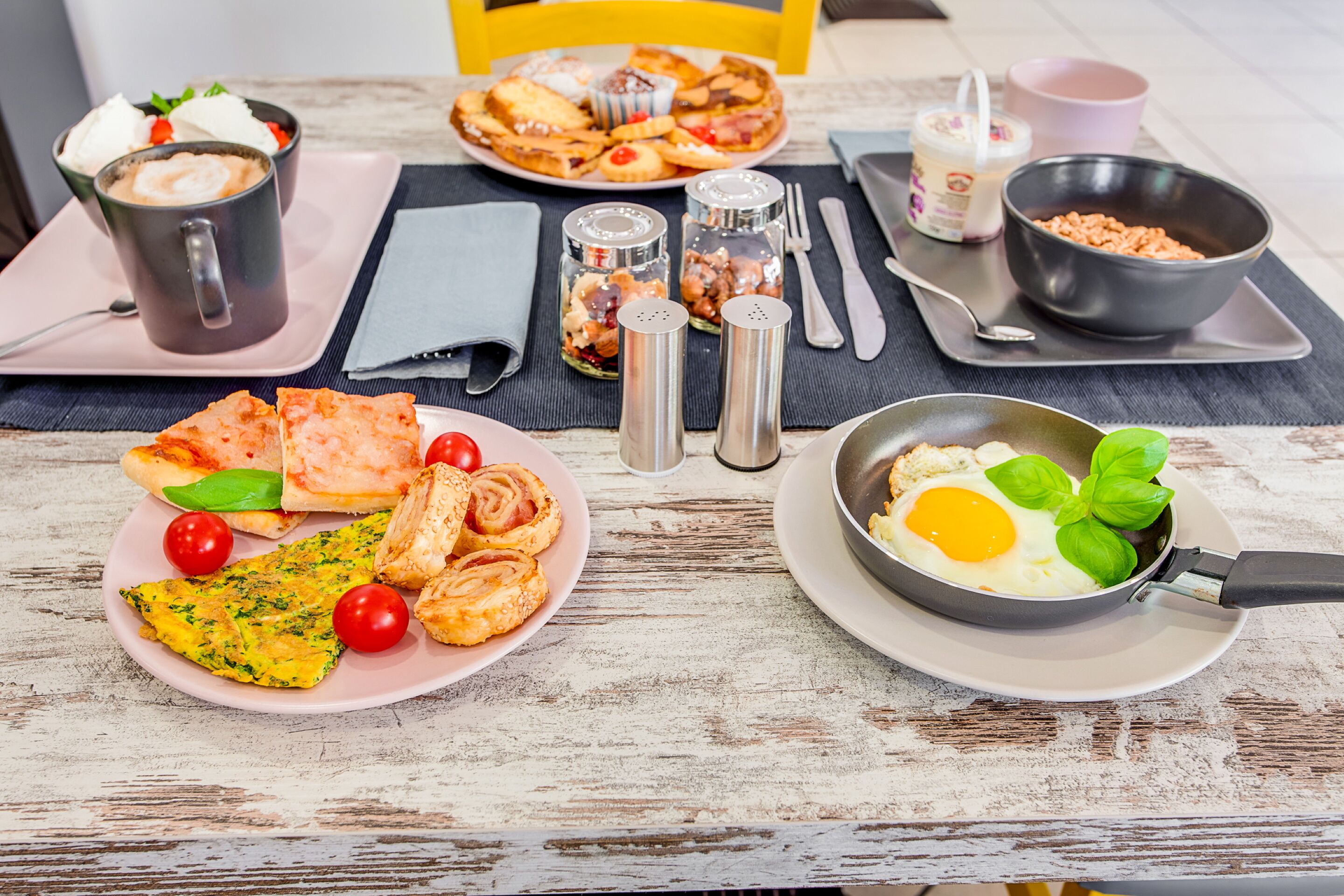 Une table de petit-déjeuner avec divers plats, notamment des œufs, des toasts et une salade de fruits.