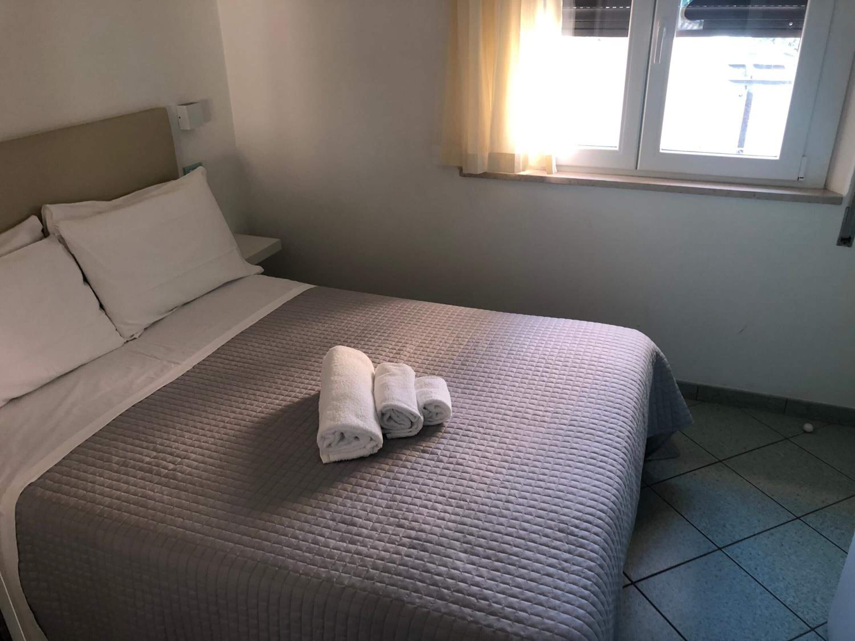 A neatly made bed with a quilted bedspread and two rolled towels on it.