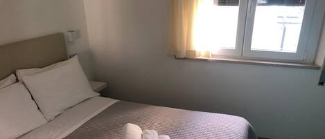 A neatly made bed with a quilted bedspread and two rolled towels on it.