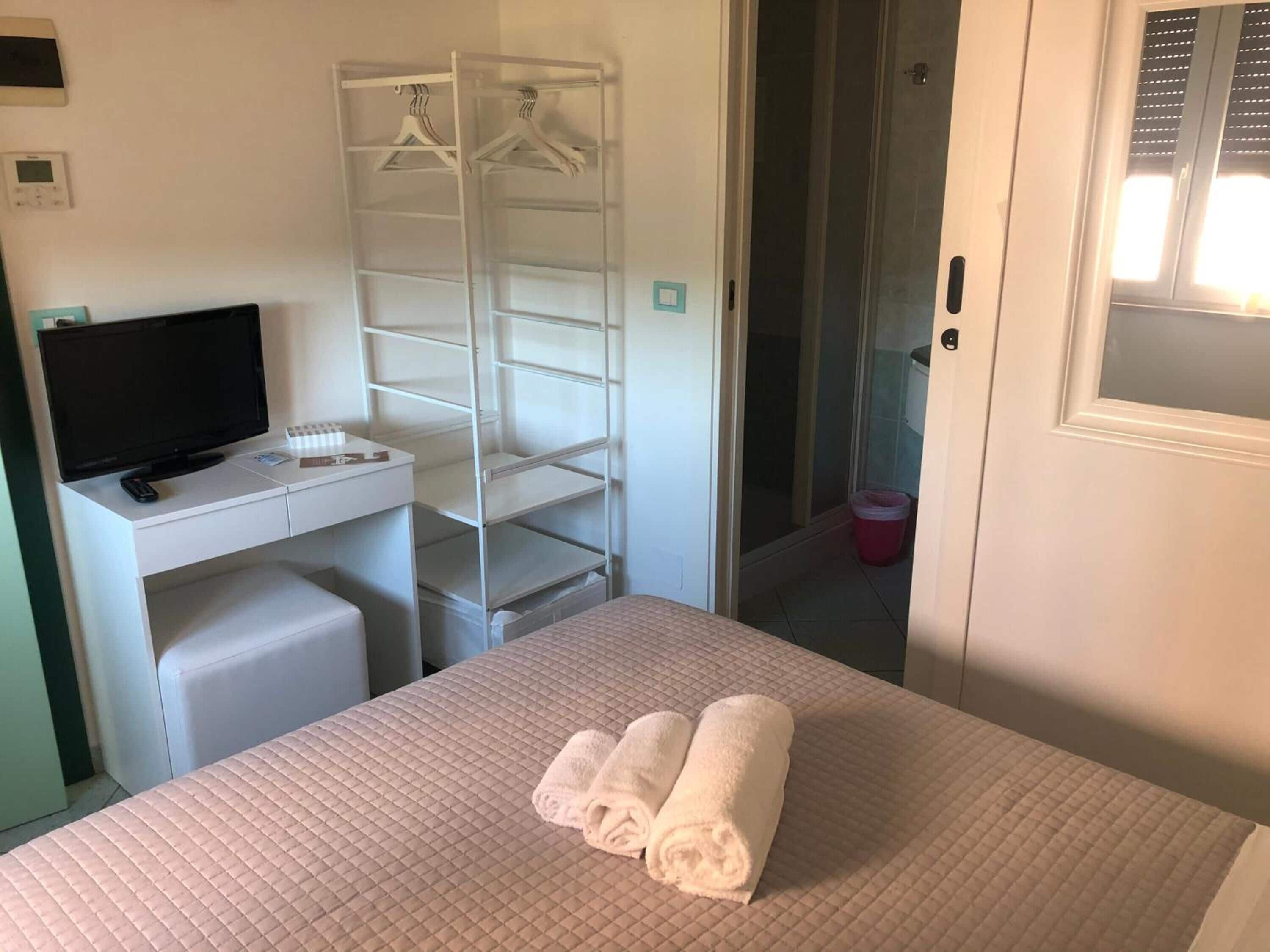 A neatly arranged hotel room with a bed, a desk with a television, a wardrobe, and a bathroom visible through an open door.