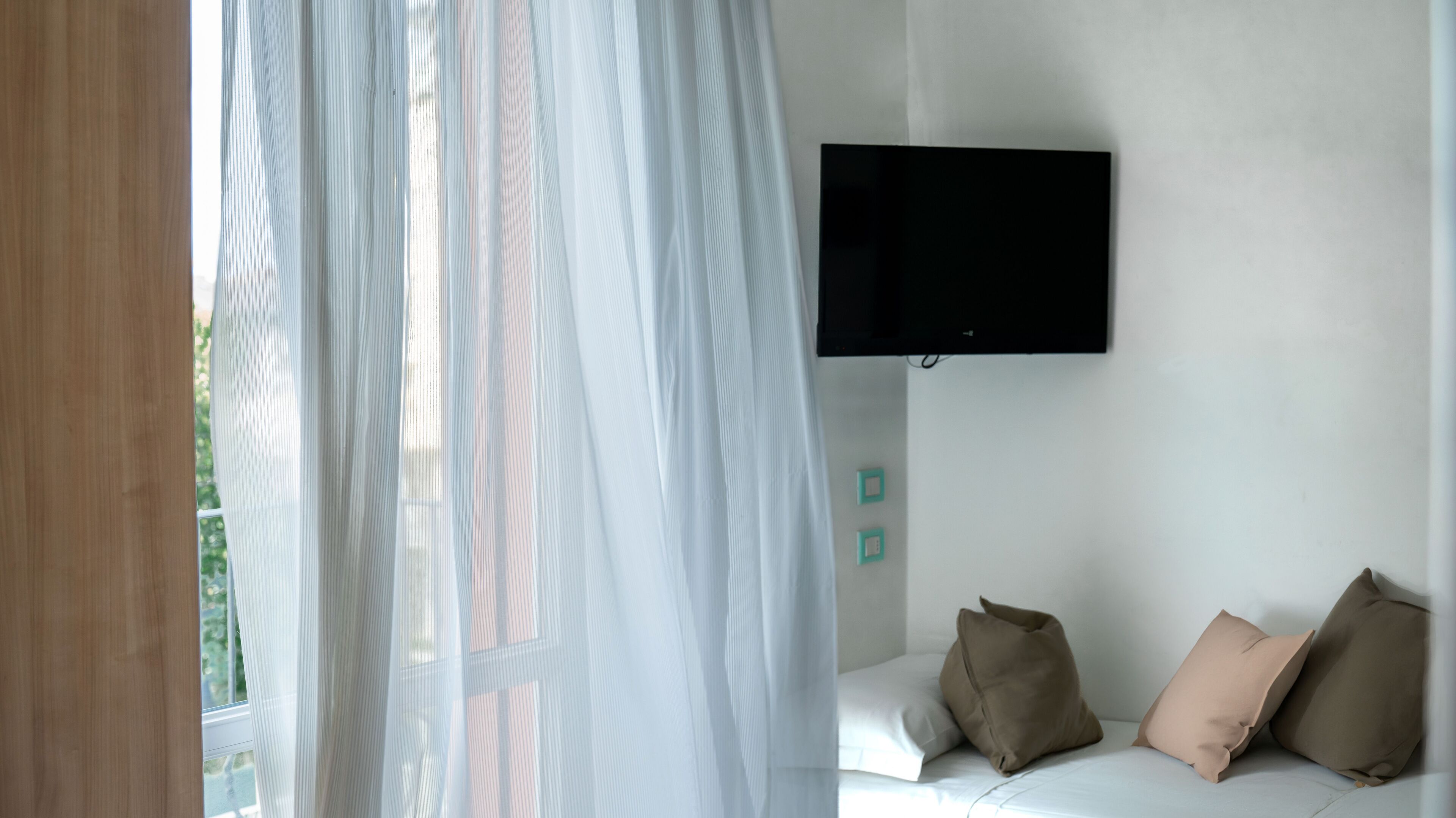 Una camera da letto con un letto, una TV a muro e tende leggere.
