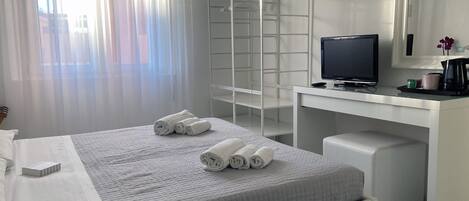 A modern hotel room with a neatly made bed, a desk with a computer, and a shower area.